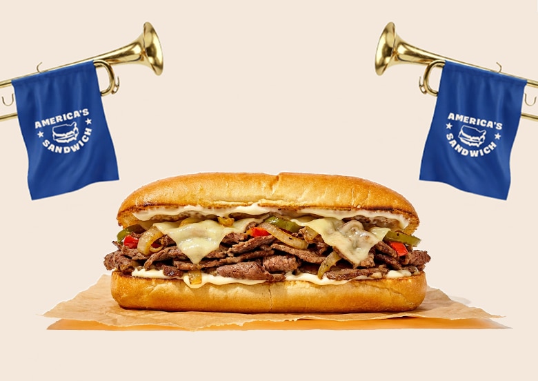 Cheesesteak sandwich topped with melted cheese, peppers, and onions, displayed between two blue 'America's Sandwich' flags.