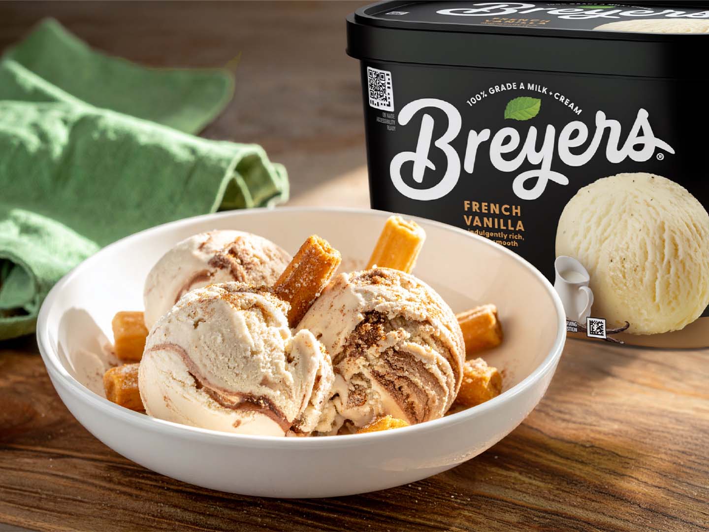 Bowl of cinnamon ice cream with churro pieces next to a tub of Breyers French Vanilla