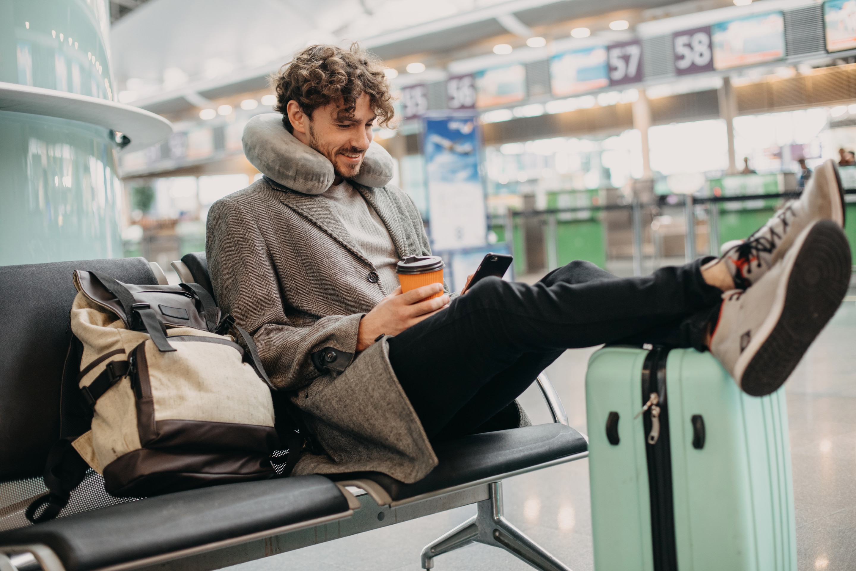 Man sitting in an airport with a coffee and suitcase who knows how to stay fresh on a long flight