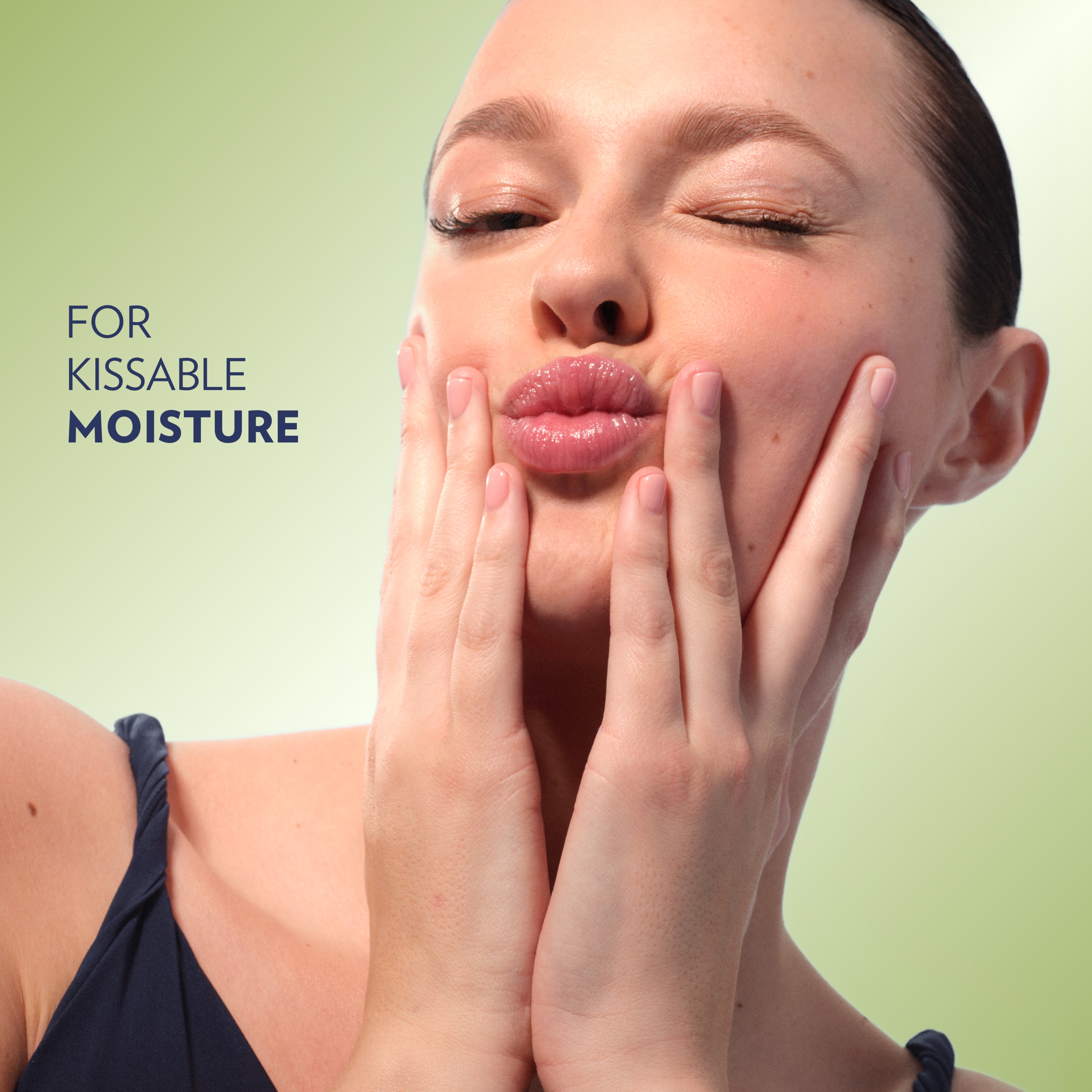 Close-up of a person with glossy lips gently pressing both hands to their cheeks against a light green background, with text
