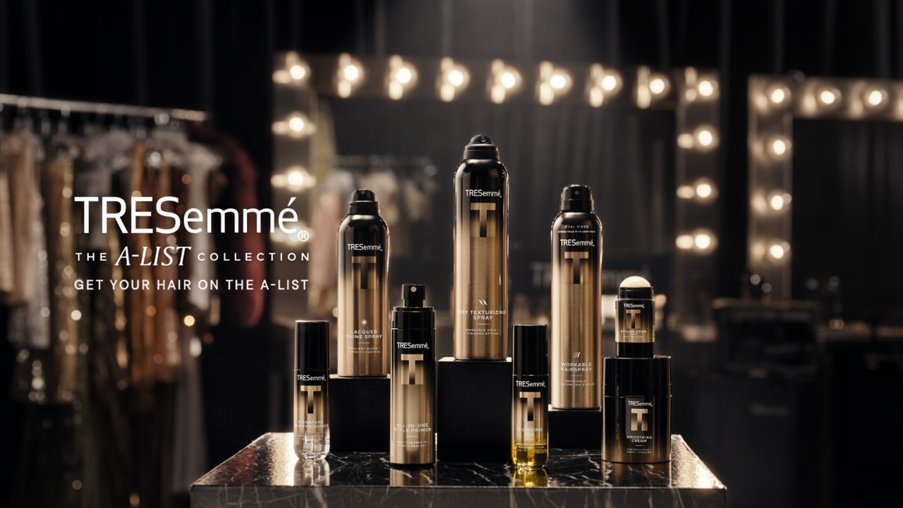 TRESemmé A-List Collection hair styling products displayed on a table in front of illuminated vanity mirrors.