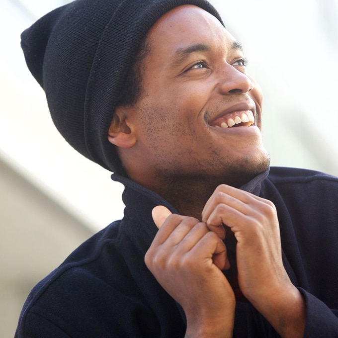 An African American man in winter hat and coat, smiling after using body wash for dry skin