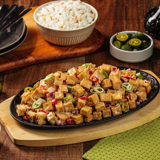 Crispy tofu sisig in a sizzling plate served with garlic rice and calamansi.