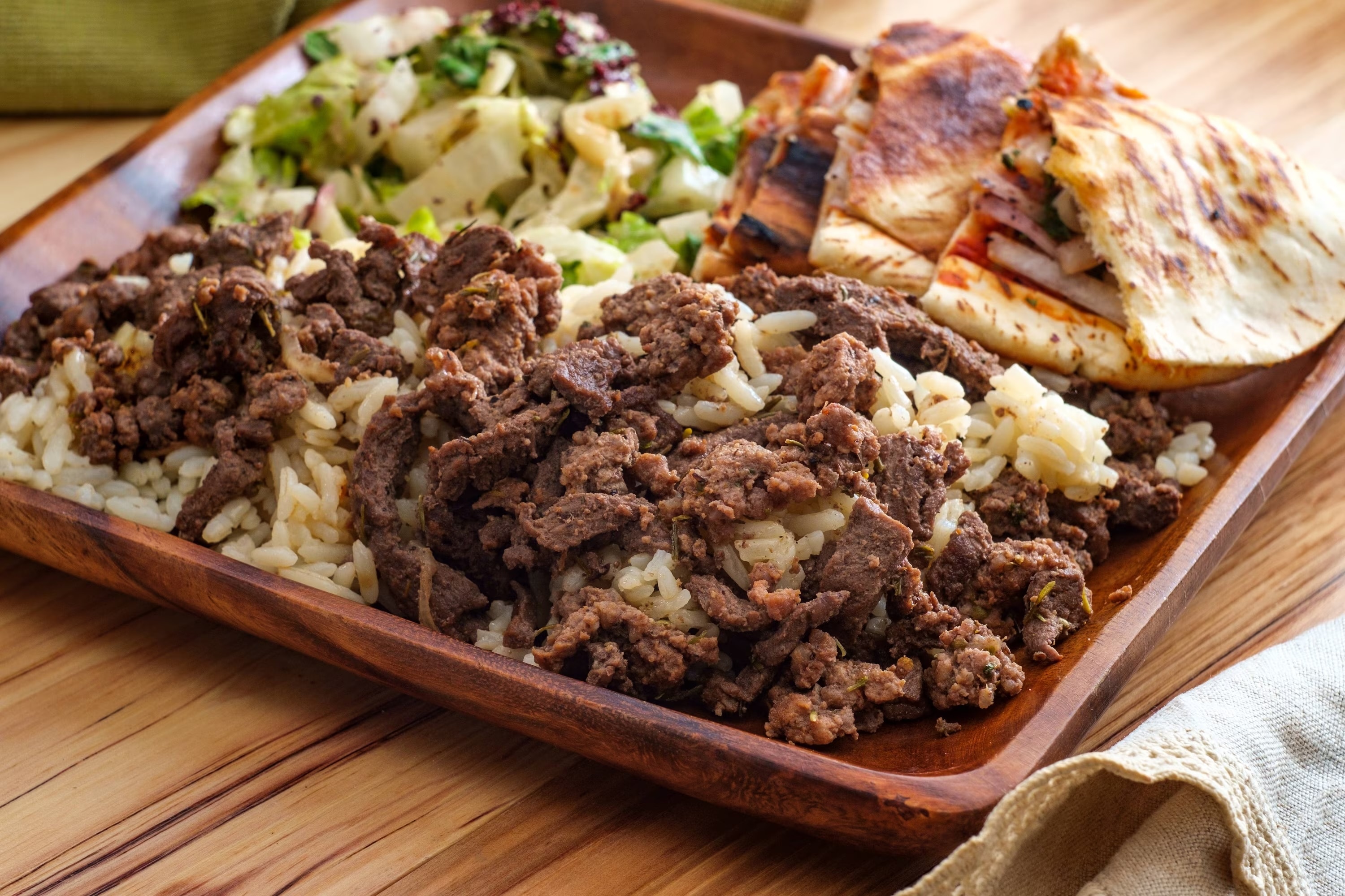 Beef shawarma served with rice, pita bread, and creamy garlic sauce.