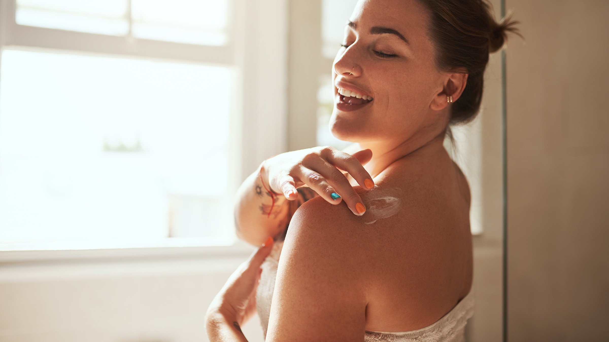 Woman applying body lotion to her shoulder in a modern bathroom setting