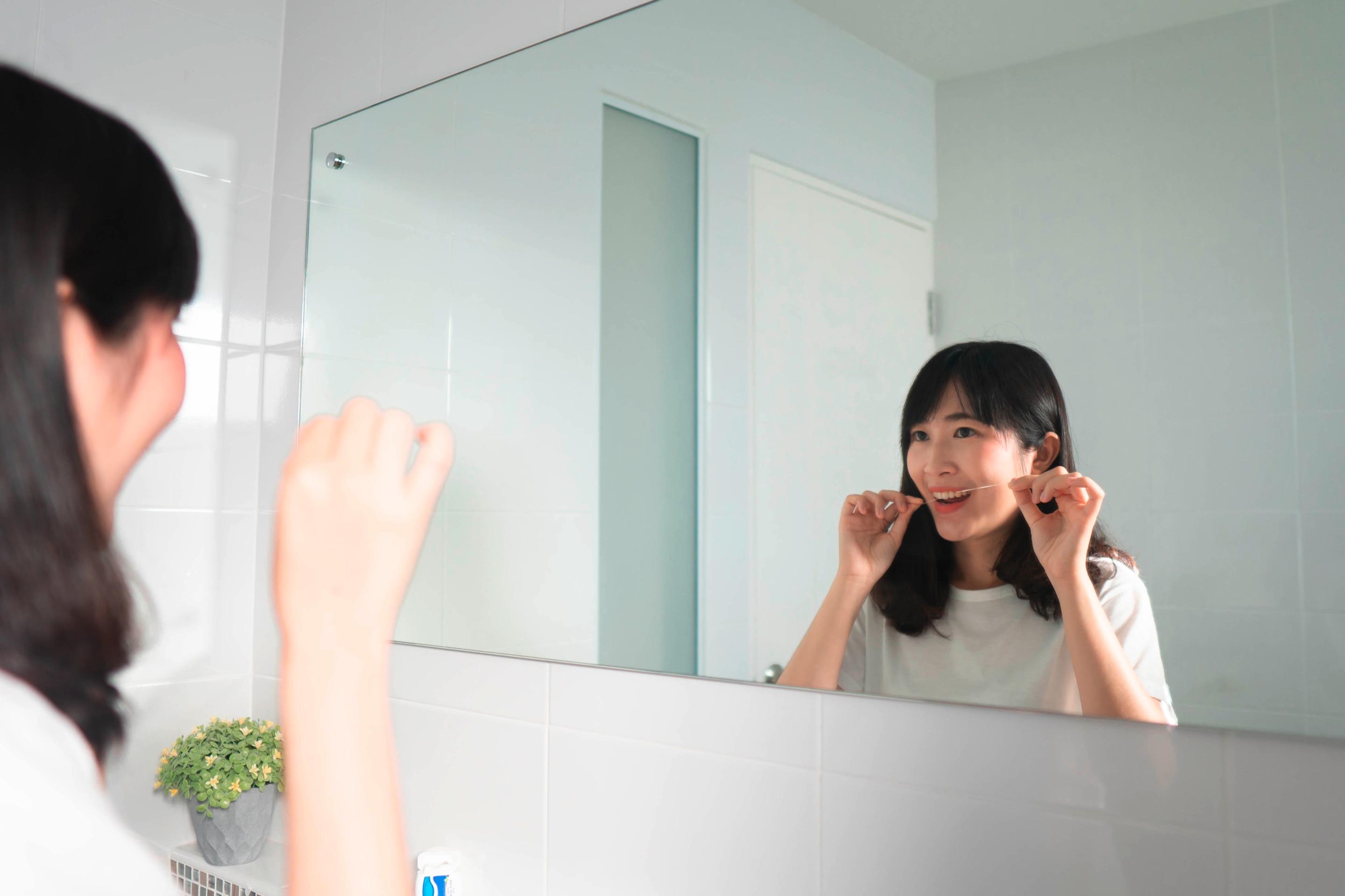 Woman flossing, looking at bathroom mirror.