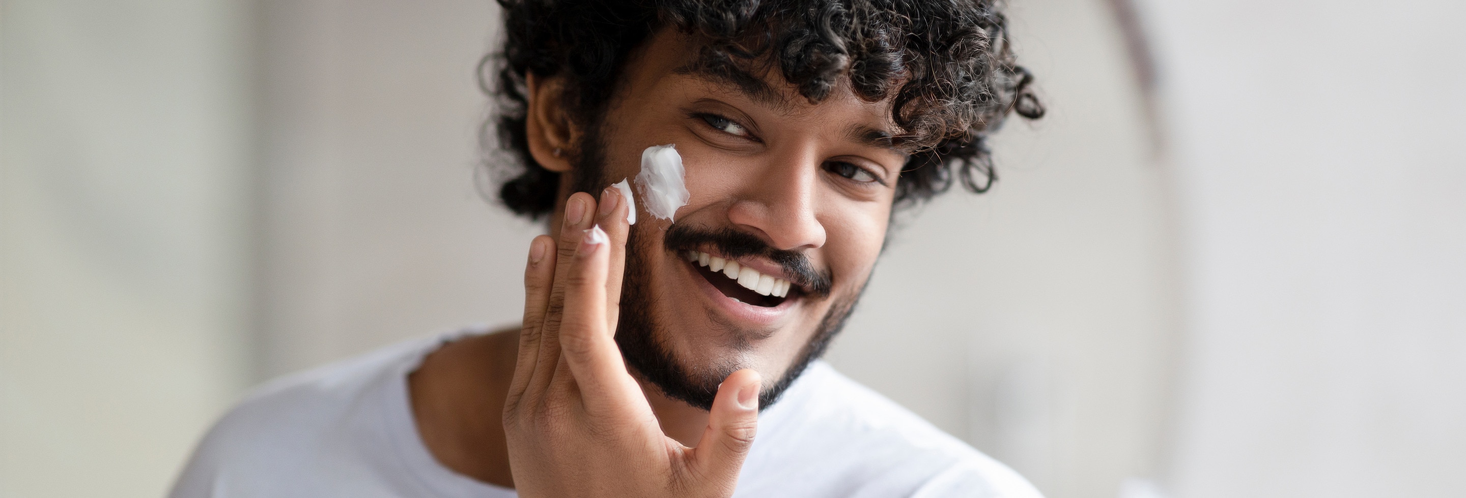 Smiling man applying facial moisturiser as part of his daily skincare routine