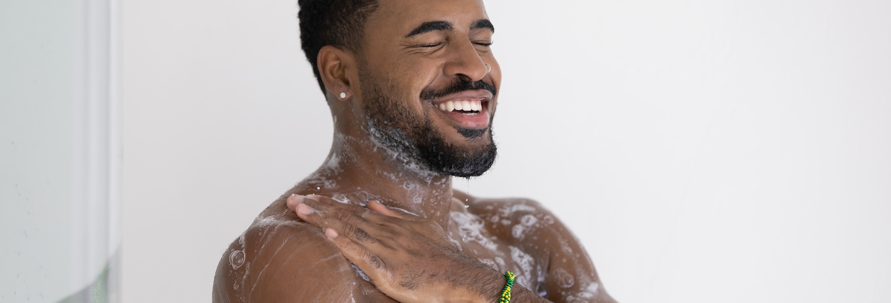  Smiling man lathering antibacterial body wash across his chest and shoulders while showering