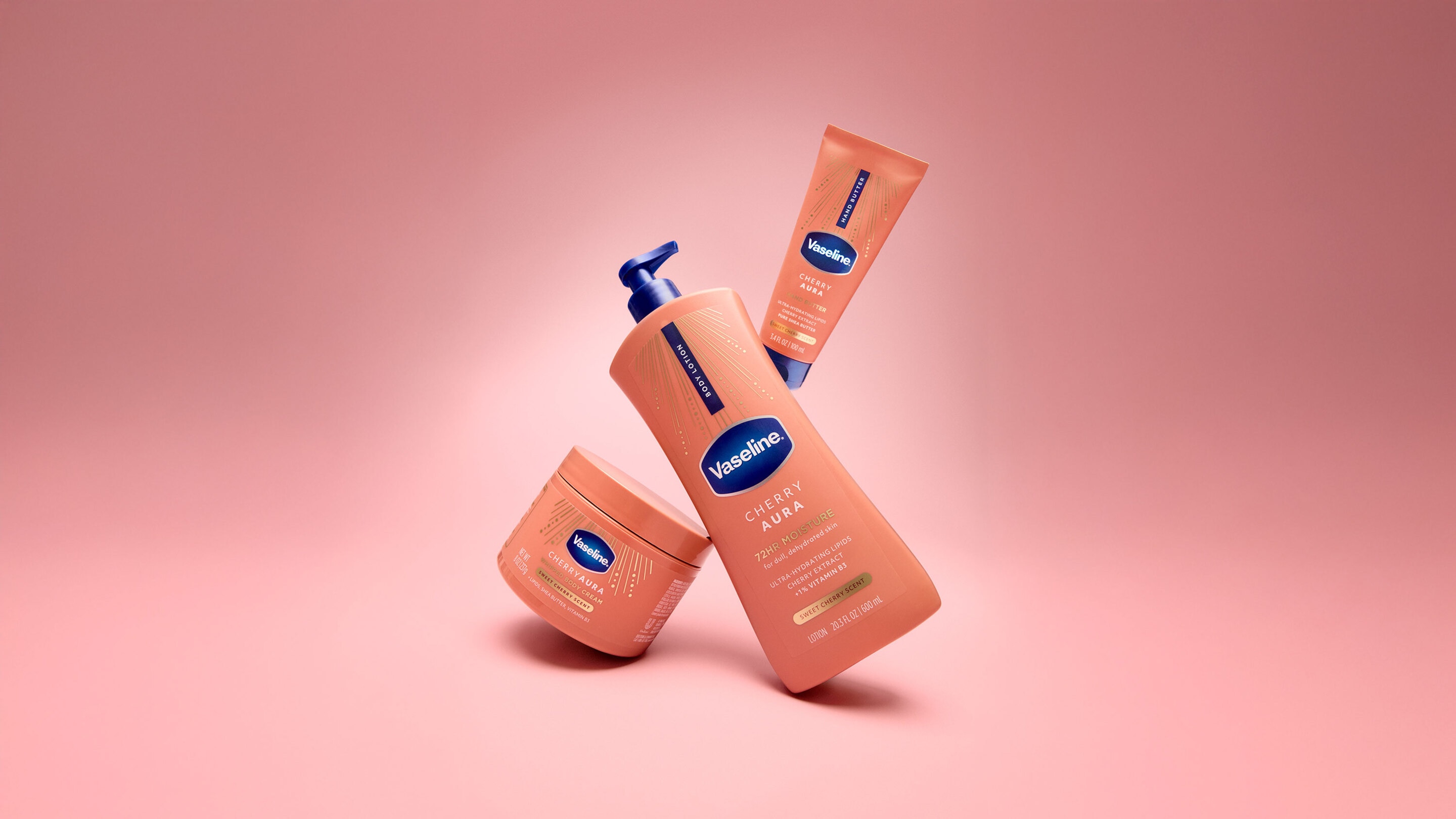 Vaseline Cherry Aura body care range, including body lotion, hand butter, and body cream, displayed on a pink background with cream swatches.