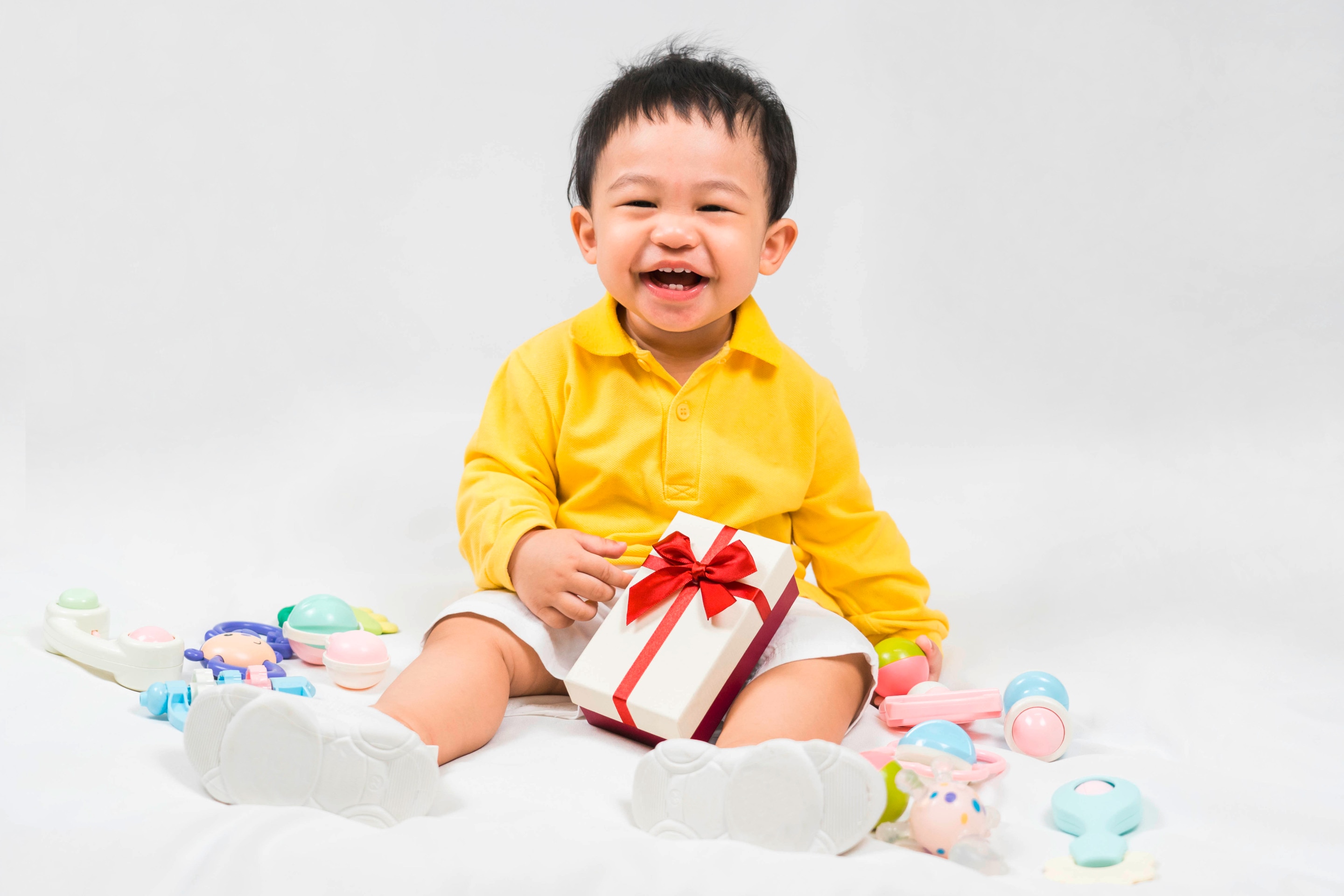 anak berusia 1 tahun berbaju kuning sedang memegang kotak kado