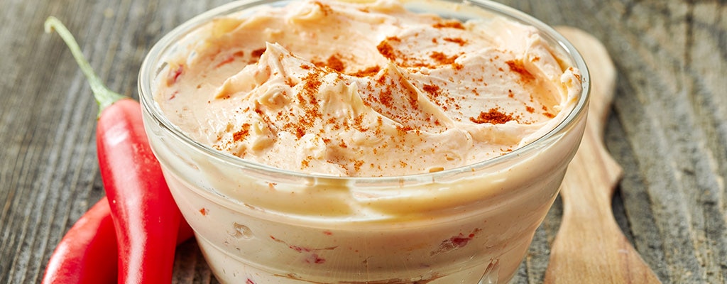 Close shot of spicy mayonnaise with chicken chunks along with red chilies and wooden spoon.