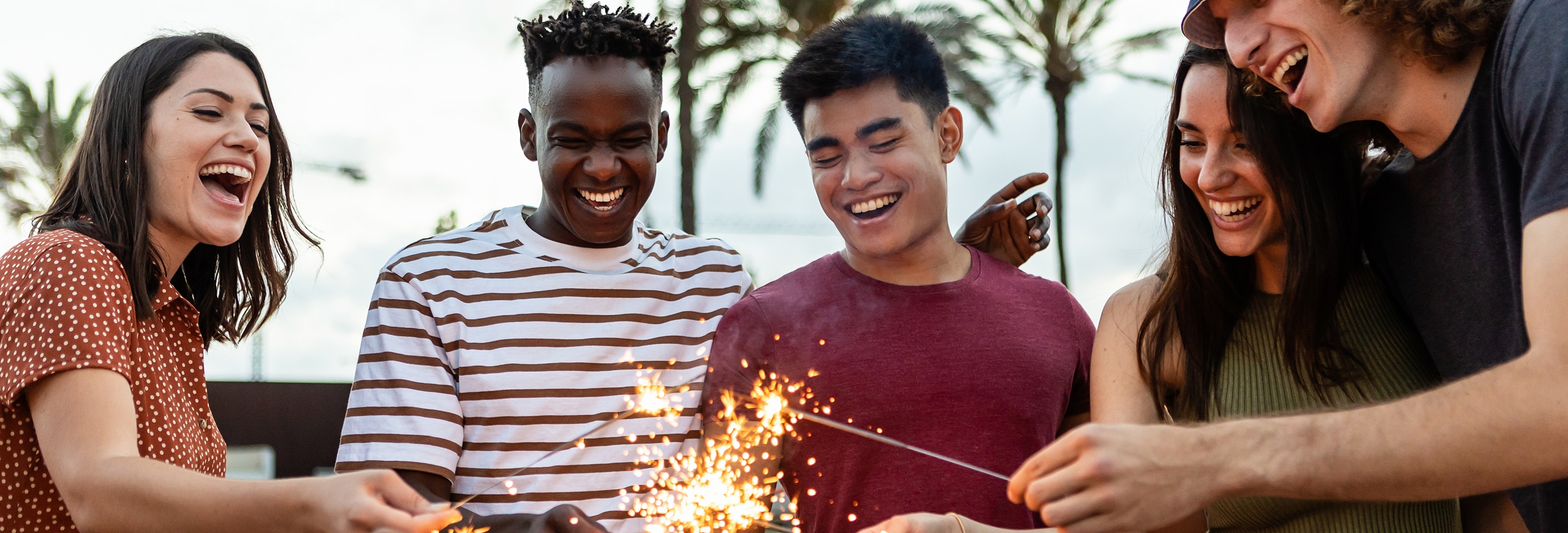 Group of friends laughing and holding sparklers outdoors to celebrate the New Year