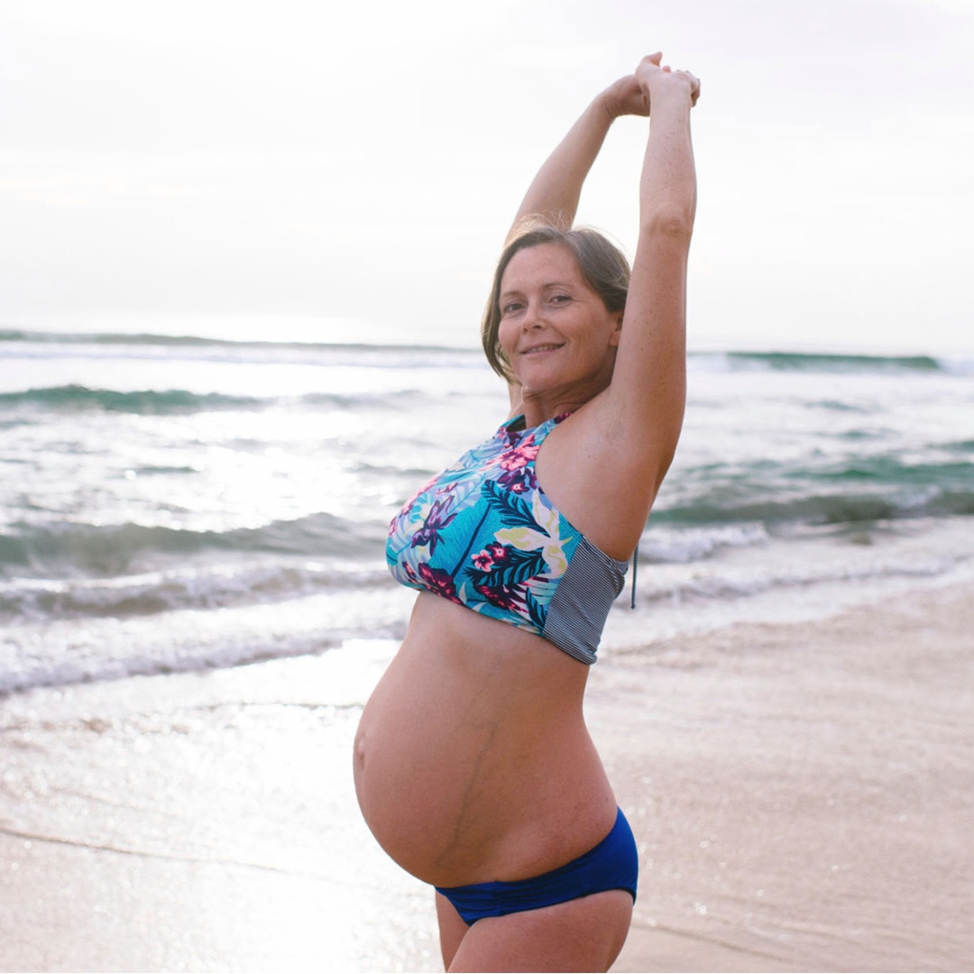 Lady standing on the beach with her pregnant belly 