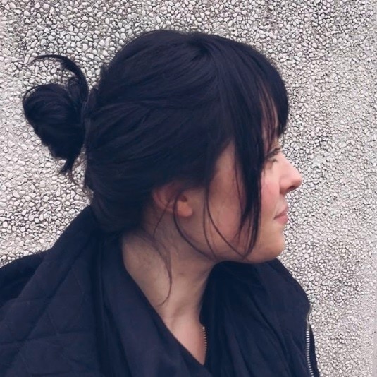 Back shot of Rihanna with sleek dark brown to grey dark hair styled into a sleek ponytail, wearing a red dress with a silver necklace on the red carpet