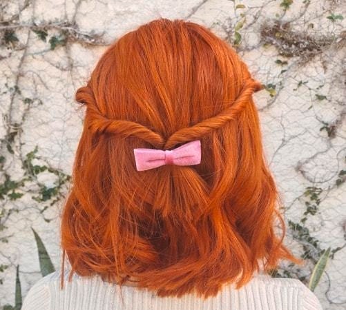 short red hairstyles: close up shot of woman with ginger hair styled into a half up half down twisted style with bow