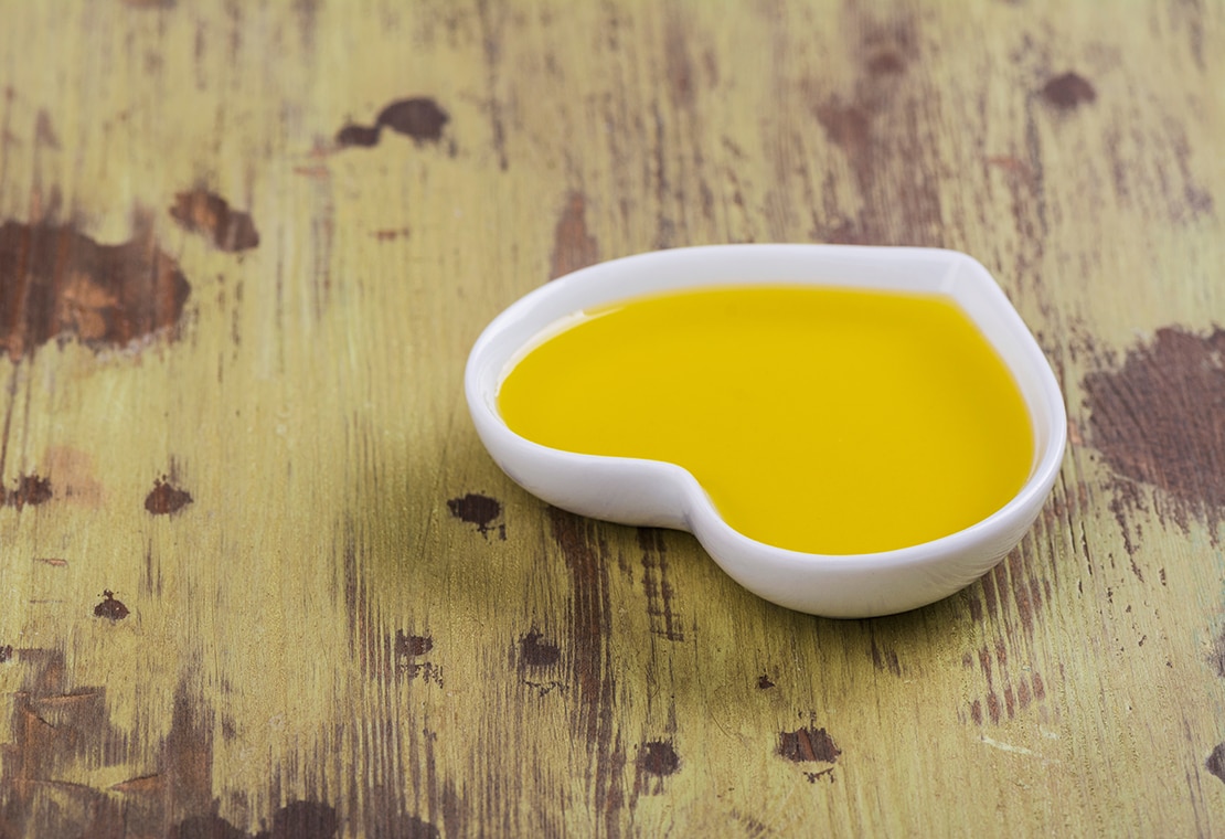 Heart-shaped dish with yellow liquid inside on a wooden surface 