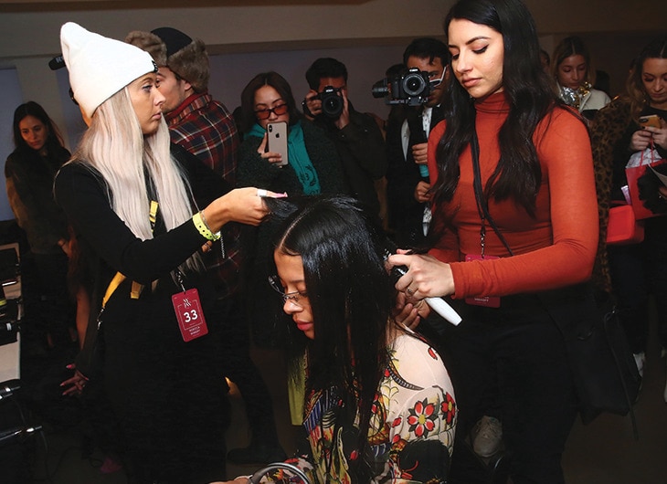 Two stylists working on a model's hair backstage.