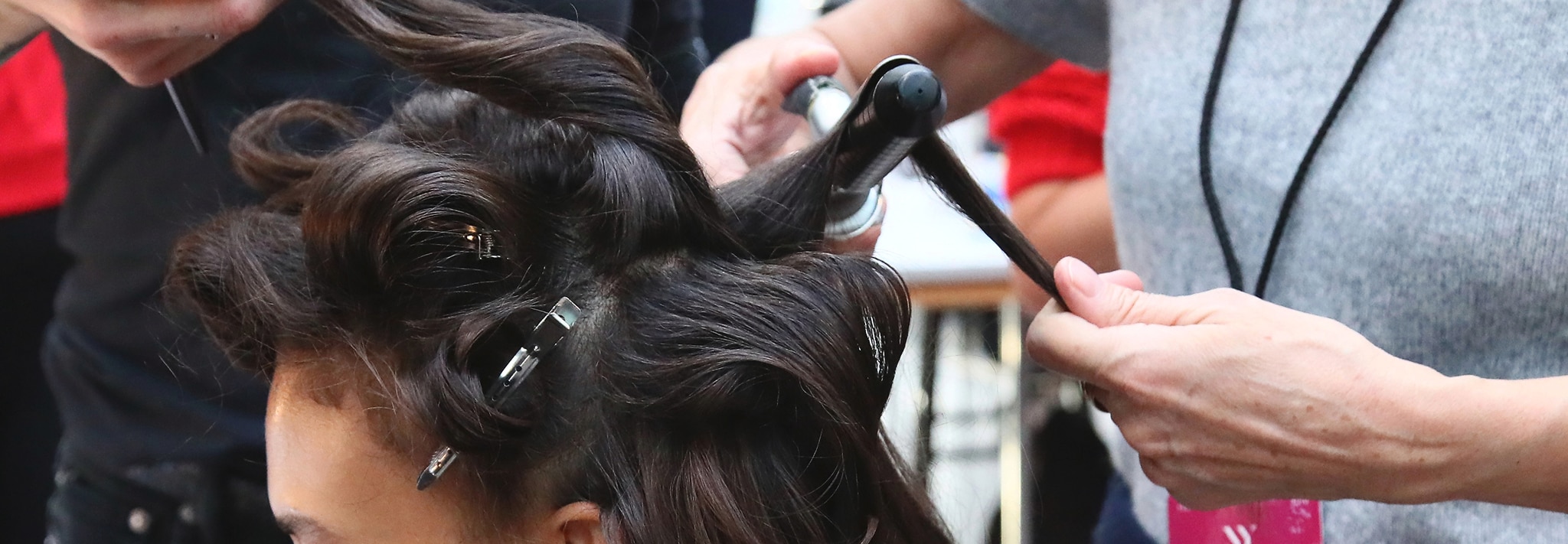 Two stylists use a brush and a hair dryer to style a woman's hair.