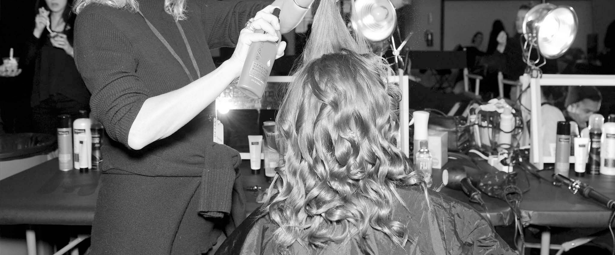 A model with curly hair getting her hair set by a stylist.