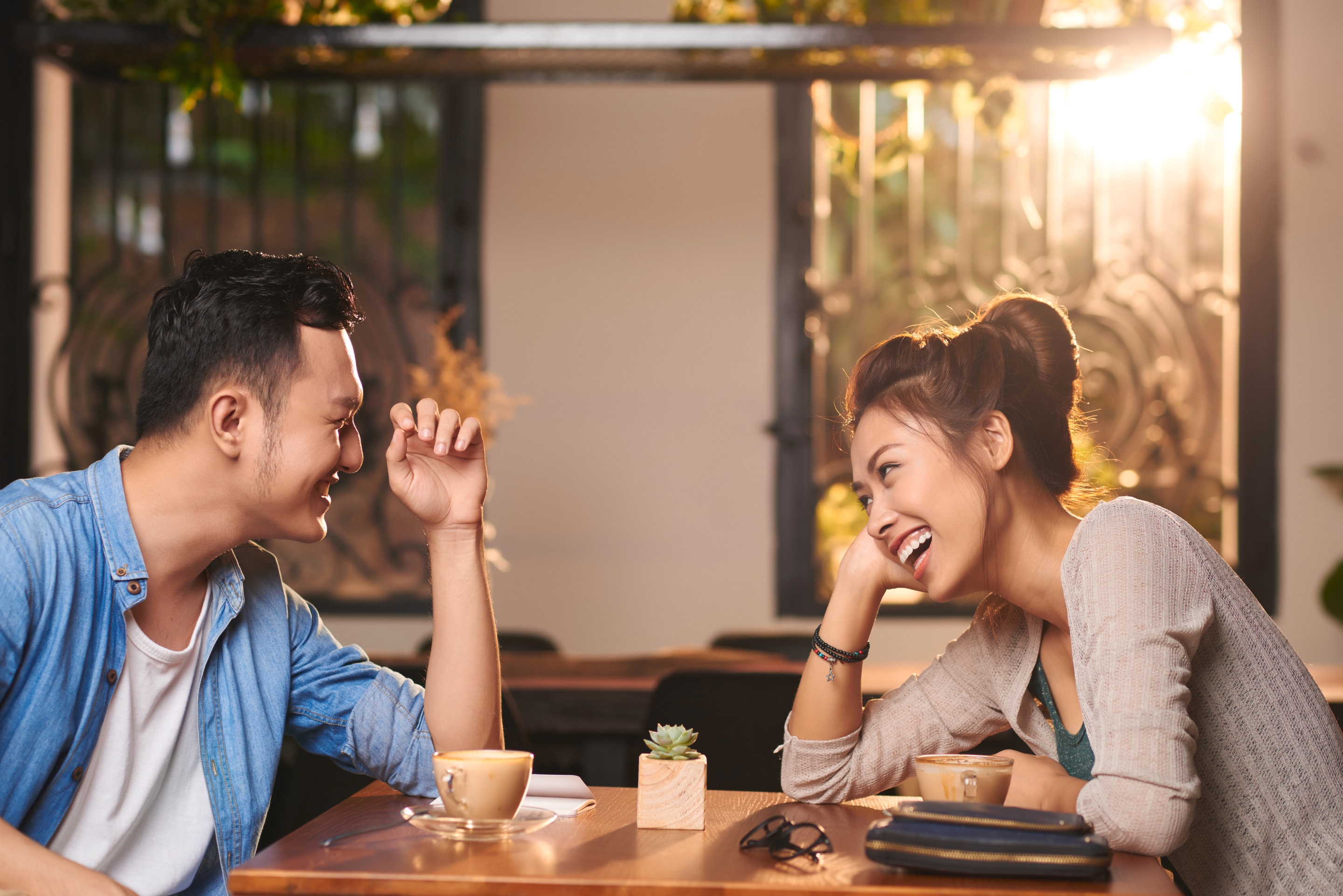 Asian couple laughing while having drinks at a coffee shop. 