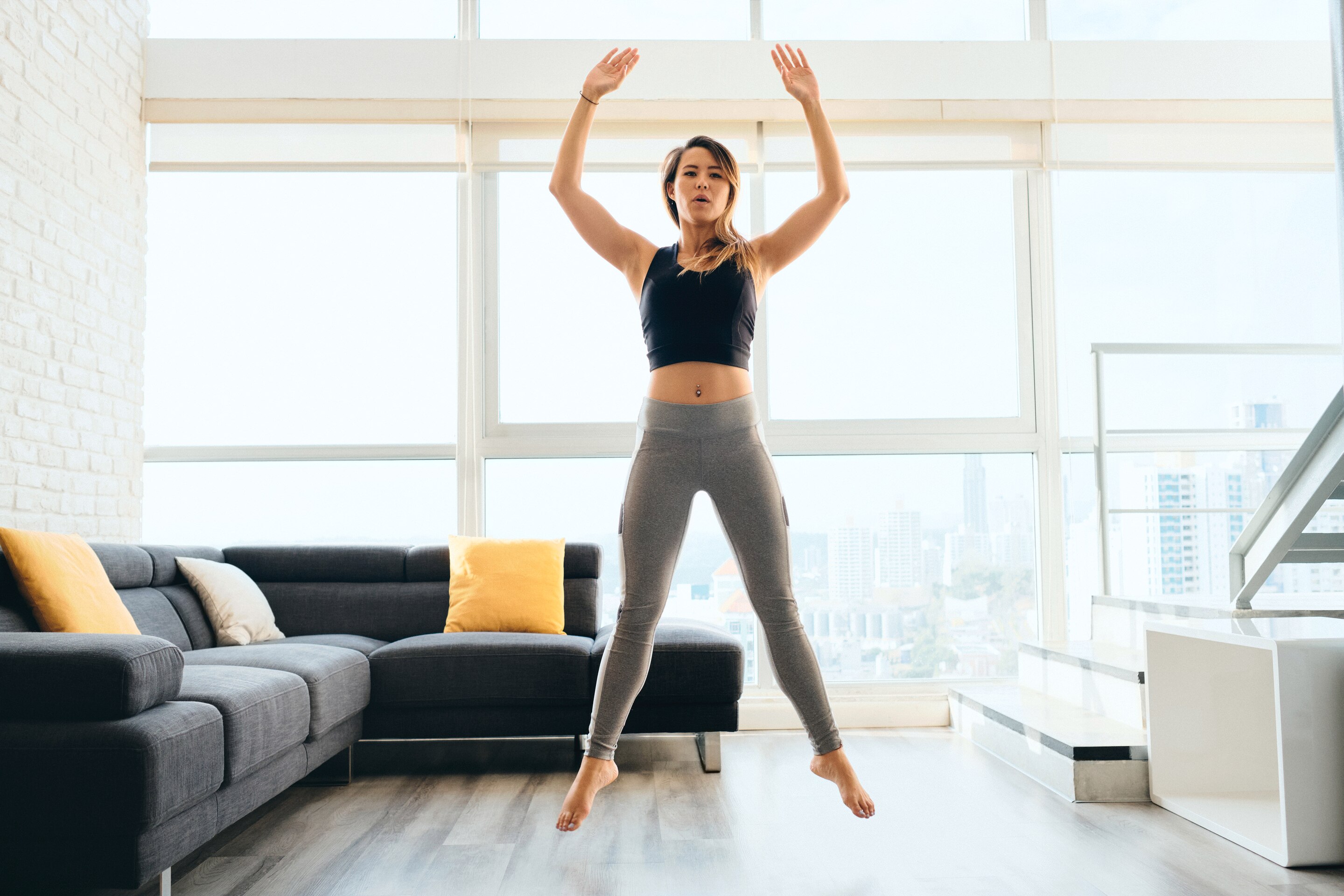 Asian woman in black and gray jumping with arms up at home