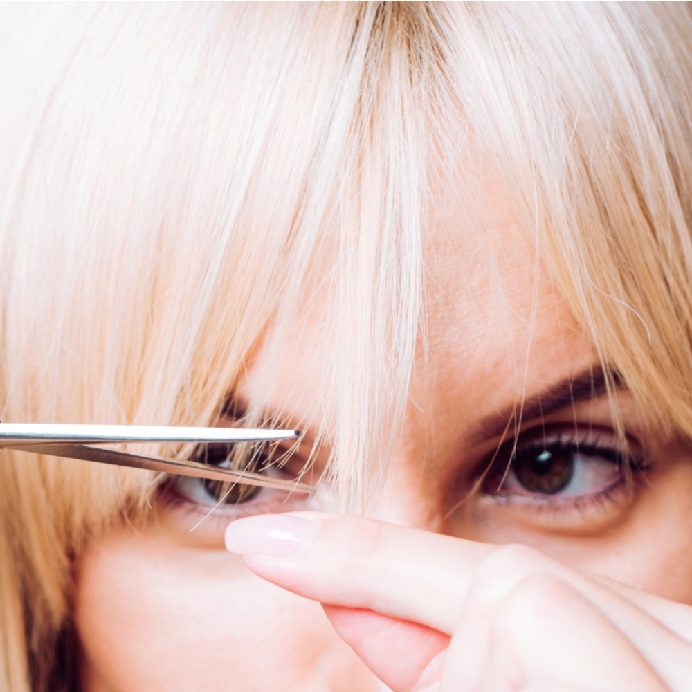Woman with blonde hair cutting her bangs with scissors. 