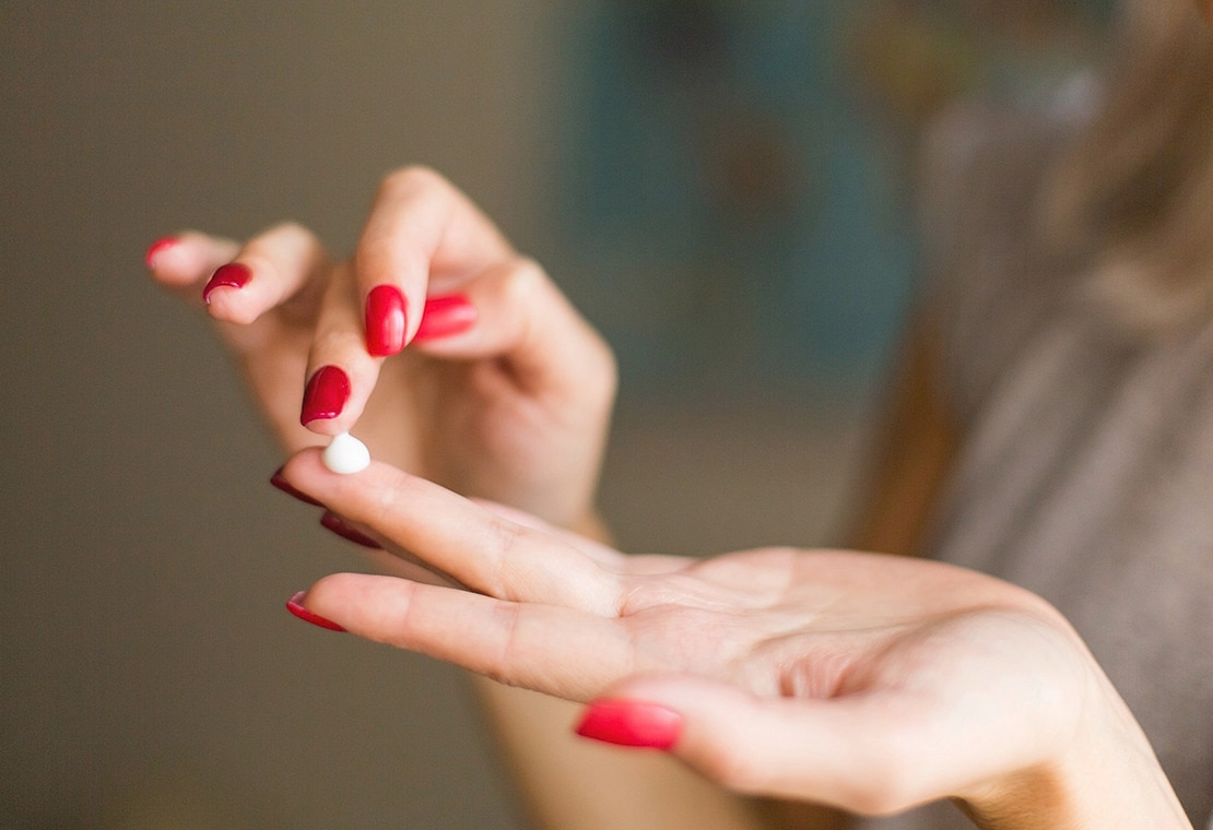 Closeup of female hands with red nail polish applying cream