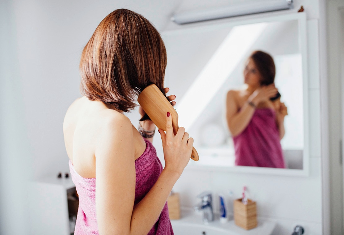 Woman with brown hair brushing her hair in front of a mirror