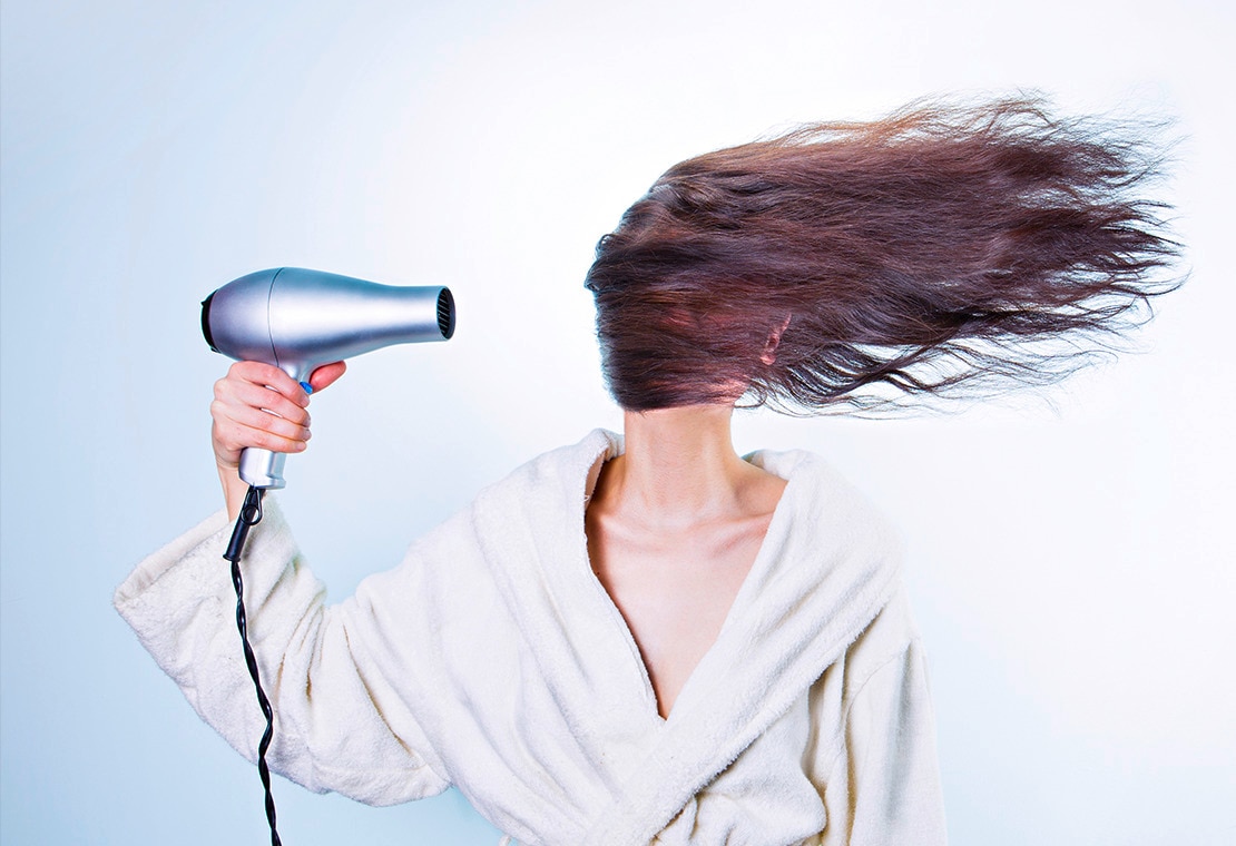 Woman in a bathrobe blow-drying her hair 