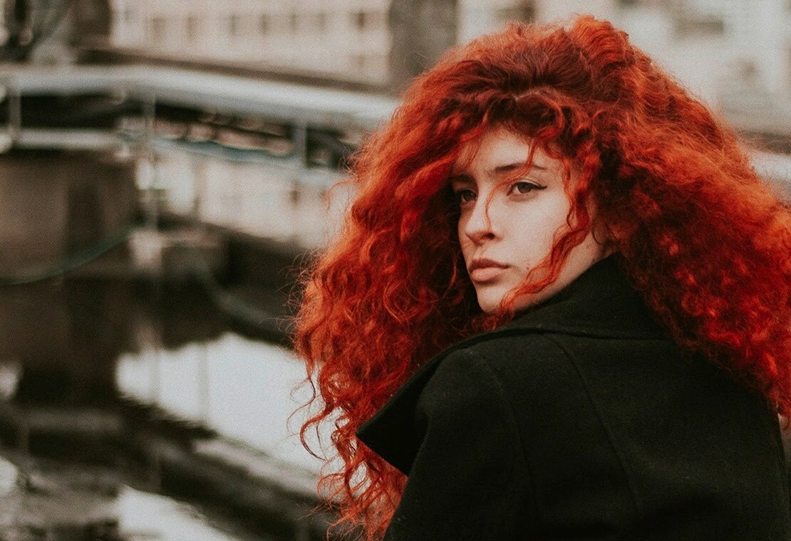 Woman with red, curly hair looking over her left shoulder