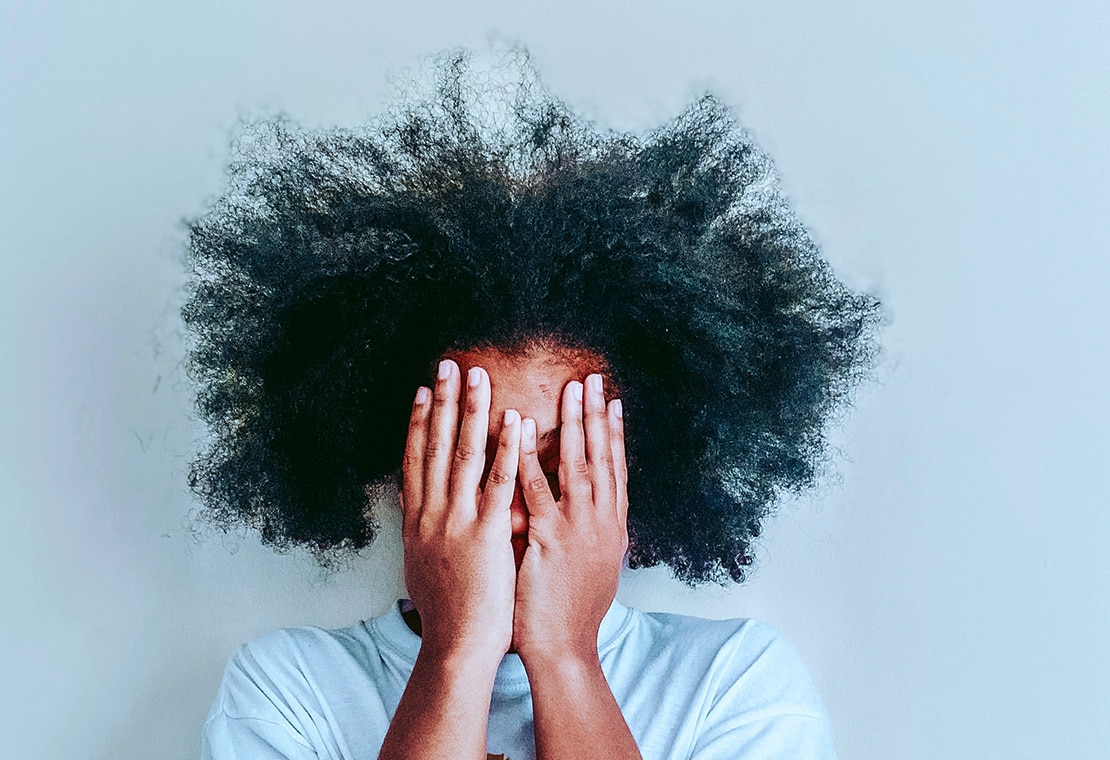 Black woman with frizzy, coily hair closing her eyes with her hands