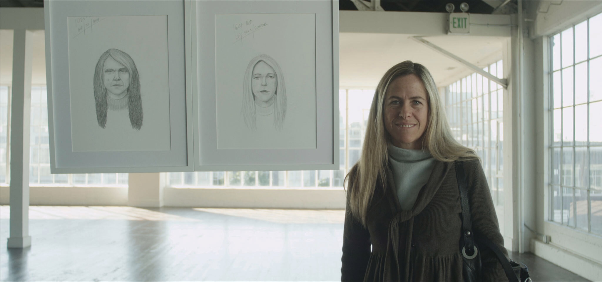 Blonde woman standing beside two potrait sketches