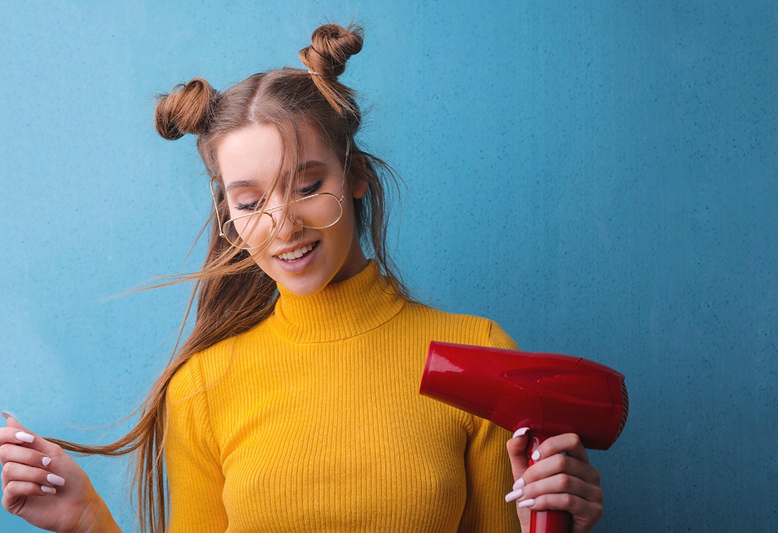 Woman in a yellow turtleneck with two hair buns holding a red hairdryer