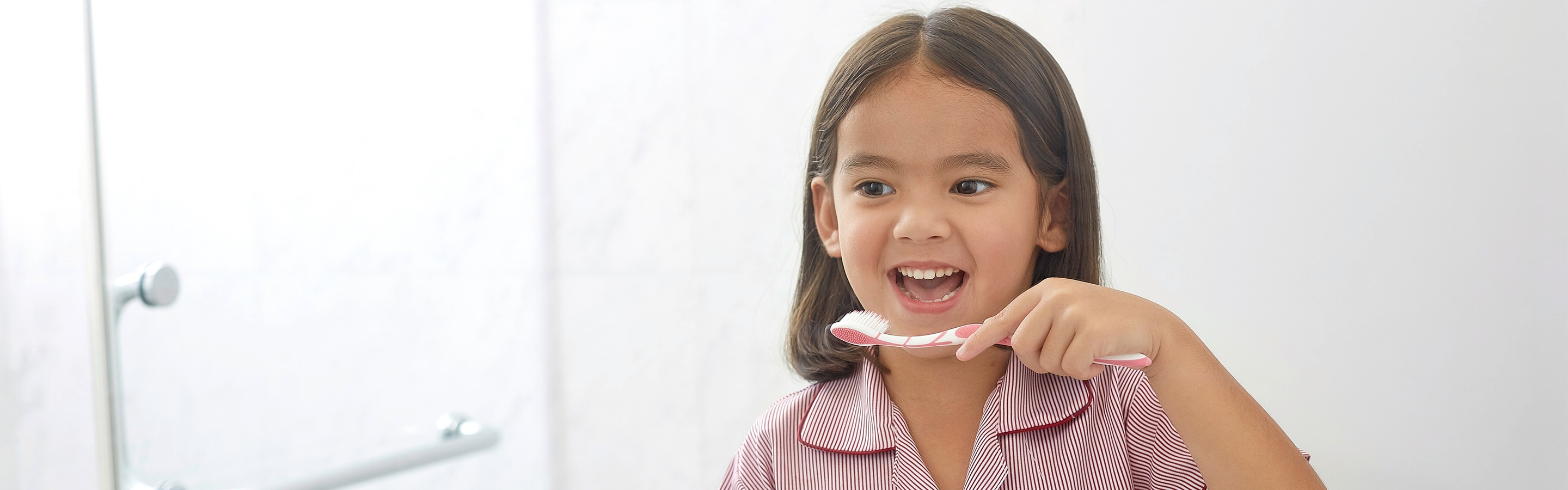 Anak kecil berkemeja garis merah dan putih menyikat gigi depan cermin