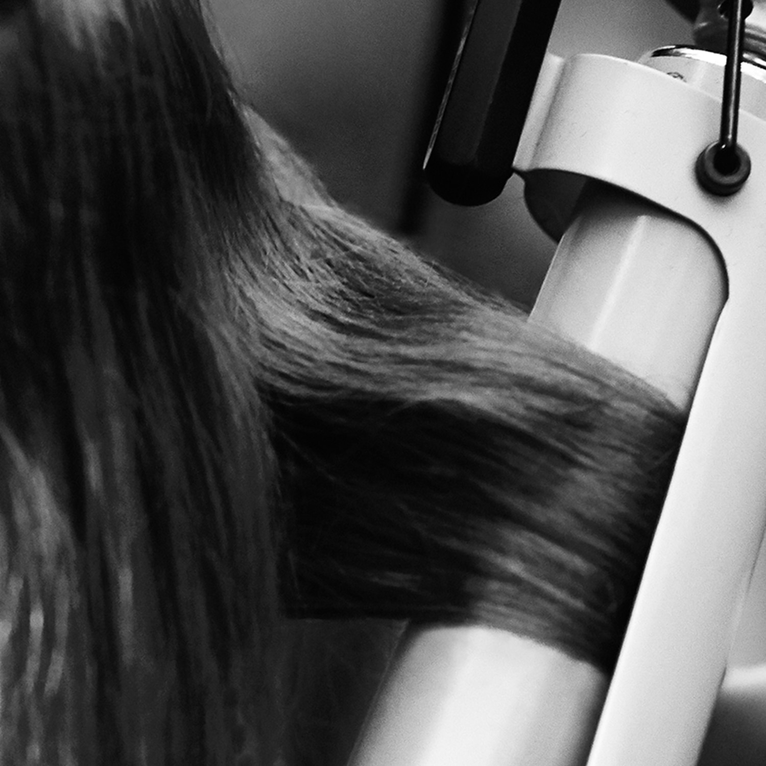 Black and white close up on the side of a model's head with a section of her hair in curling tongs and a stylist's hand just visible