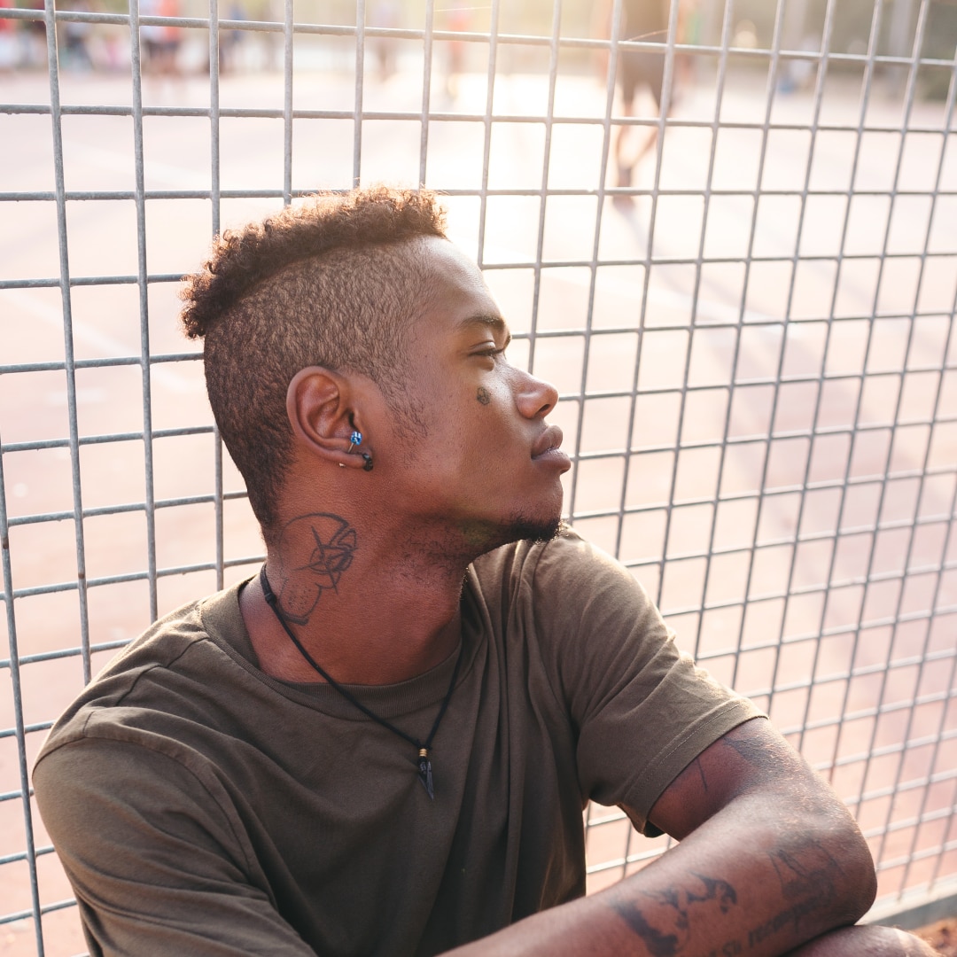 chico con tatuajes junto a una valla
