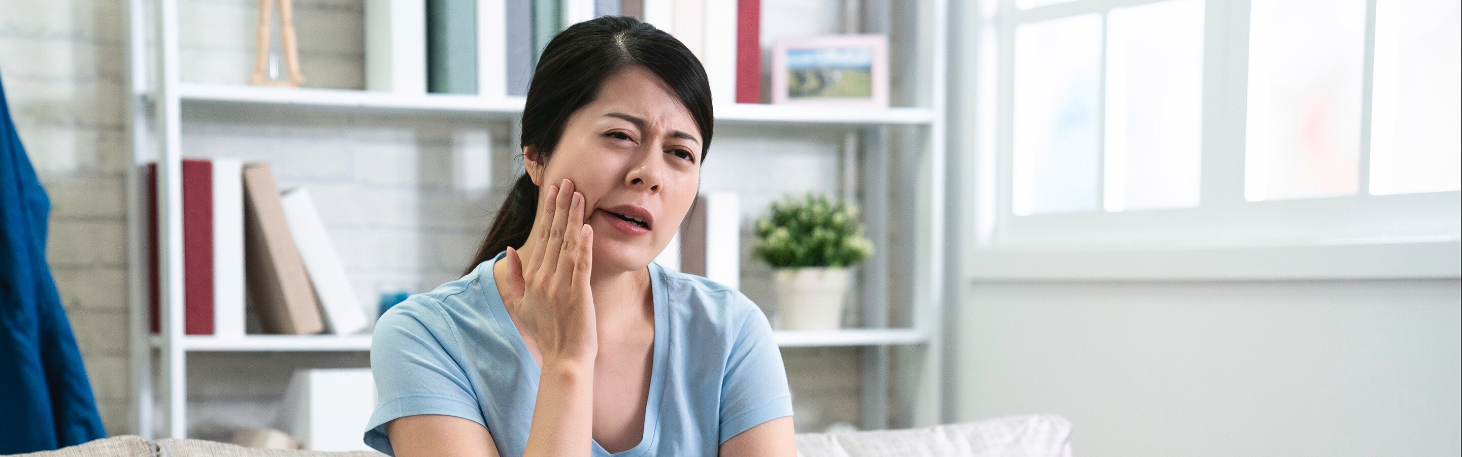 Perempuan sedang memegang pipi akibat gusi bengkak.