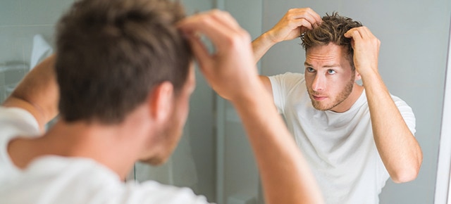 Homem em frente ao espelho checando o couro cabeludo