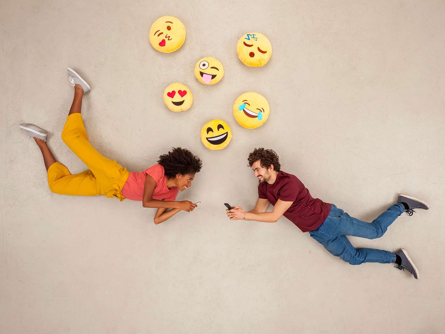 a young guy and girl laying on the floor with emoji pillows