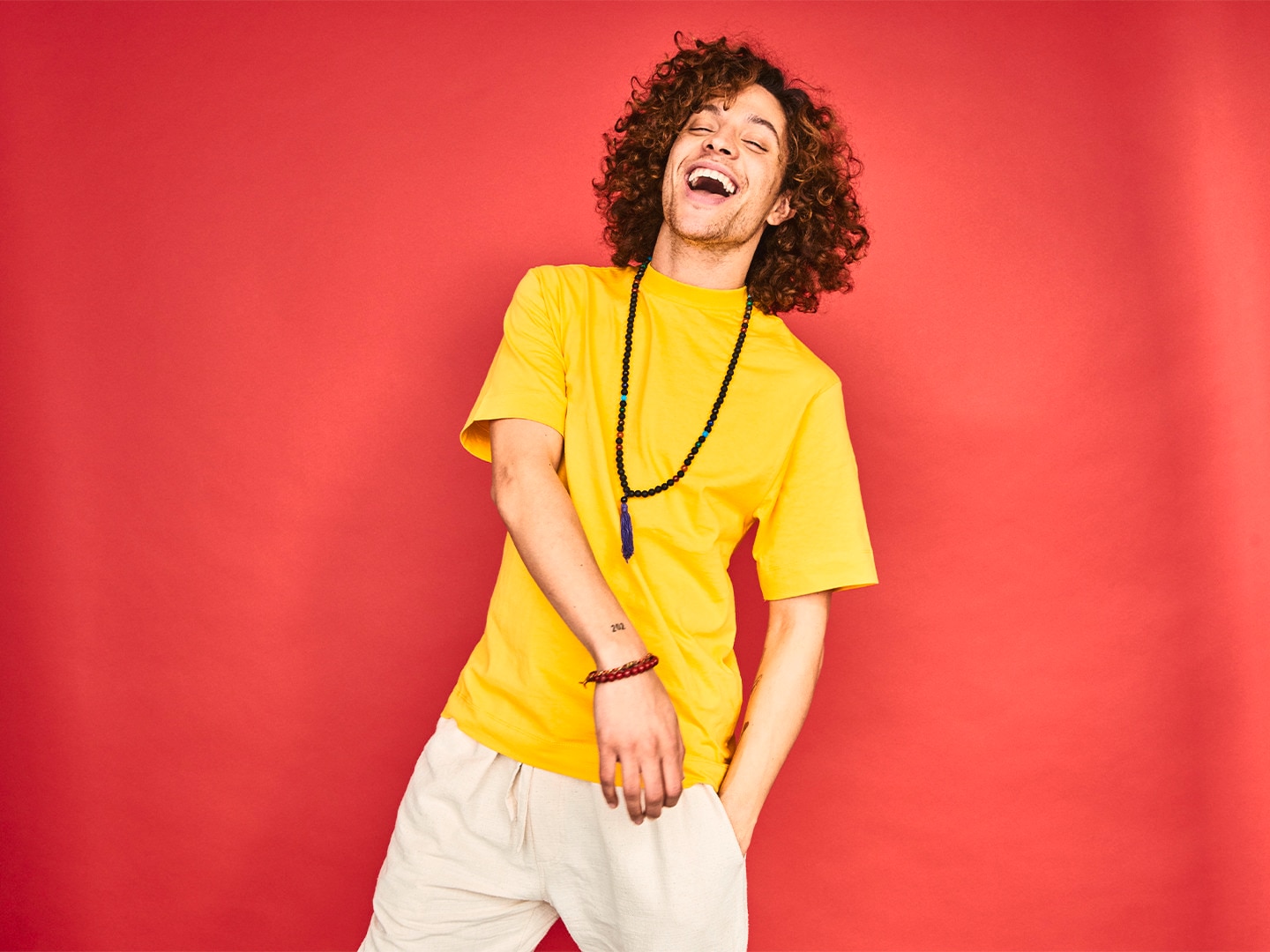 Guy in yellow shirt laughing against red backdrop
