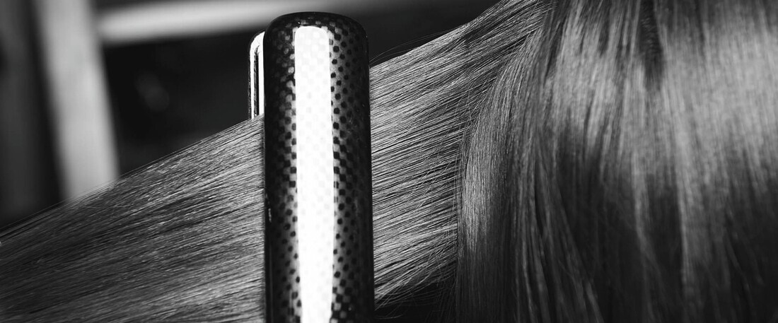 A section of long dark, damaged hair being styled with a flat iron