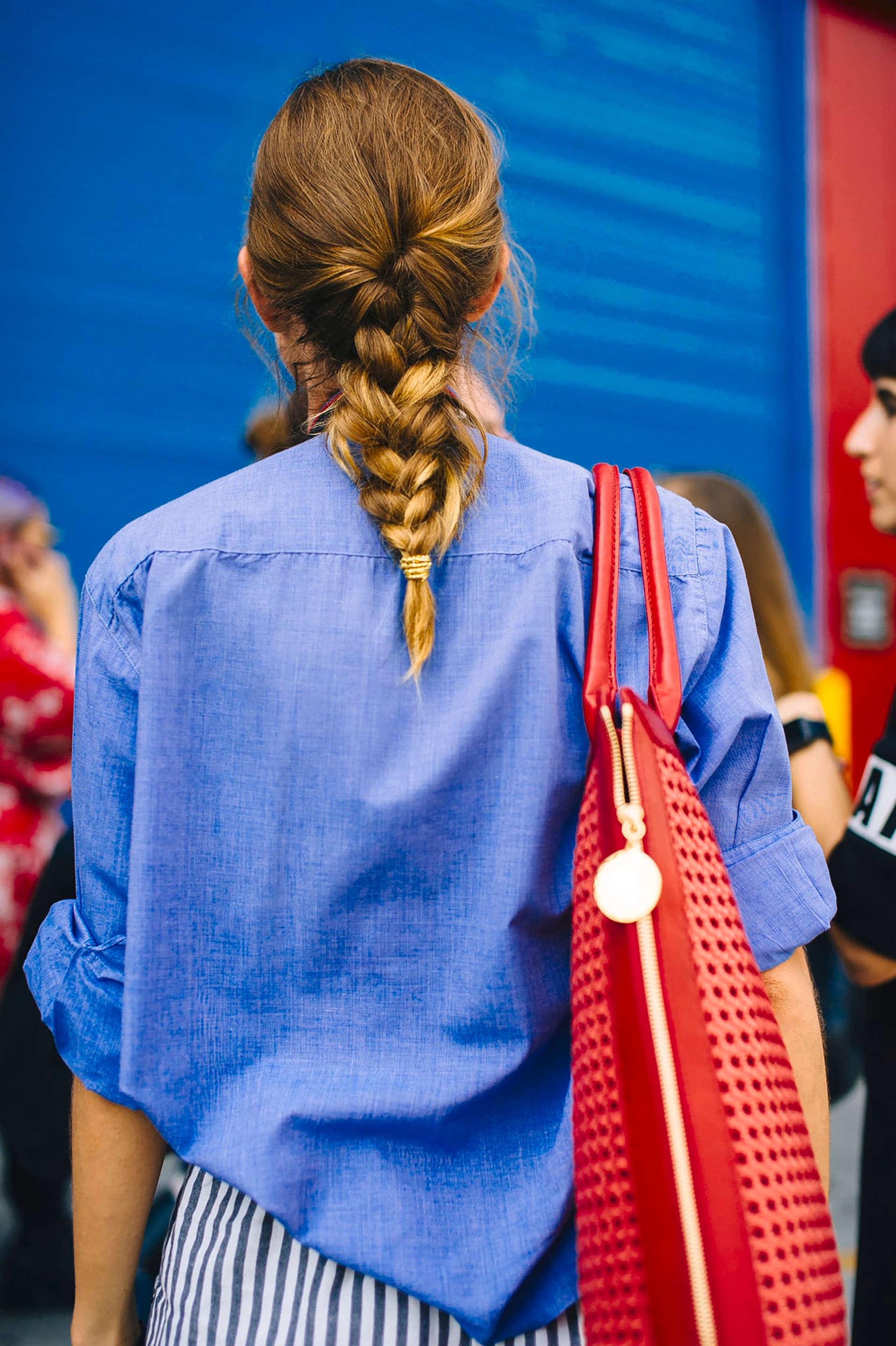A woman standing in the street wearing a blue shirt with her hair in a thick braid