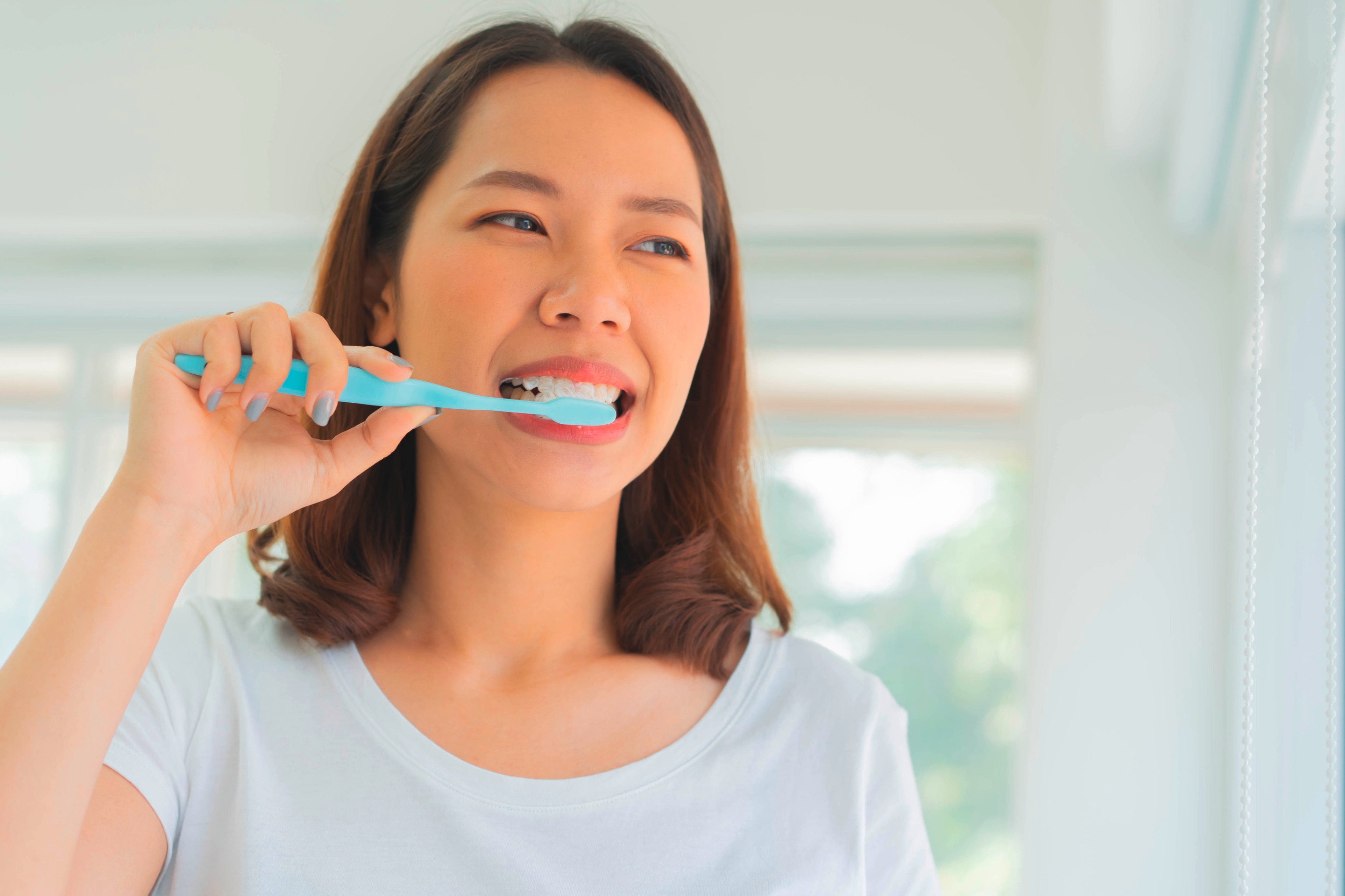 Woman brushing her teeth with a blue toothbrush.