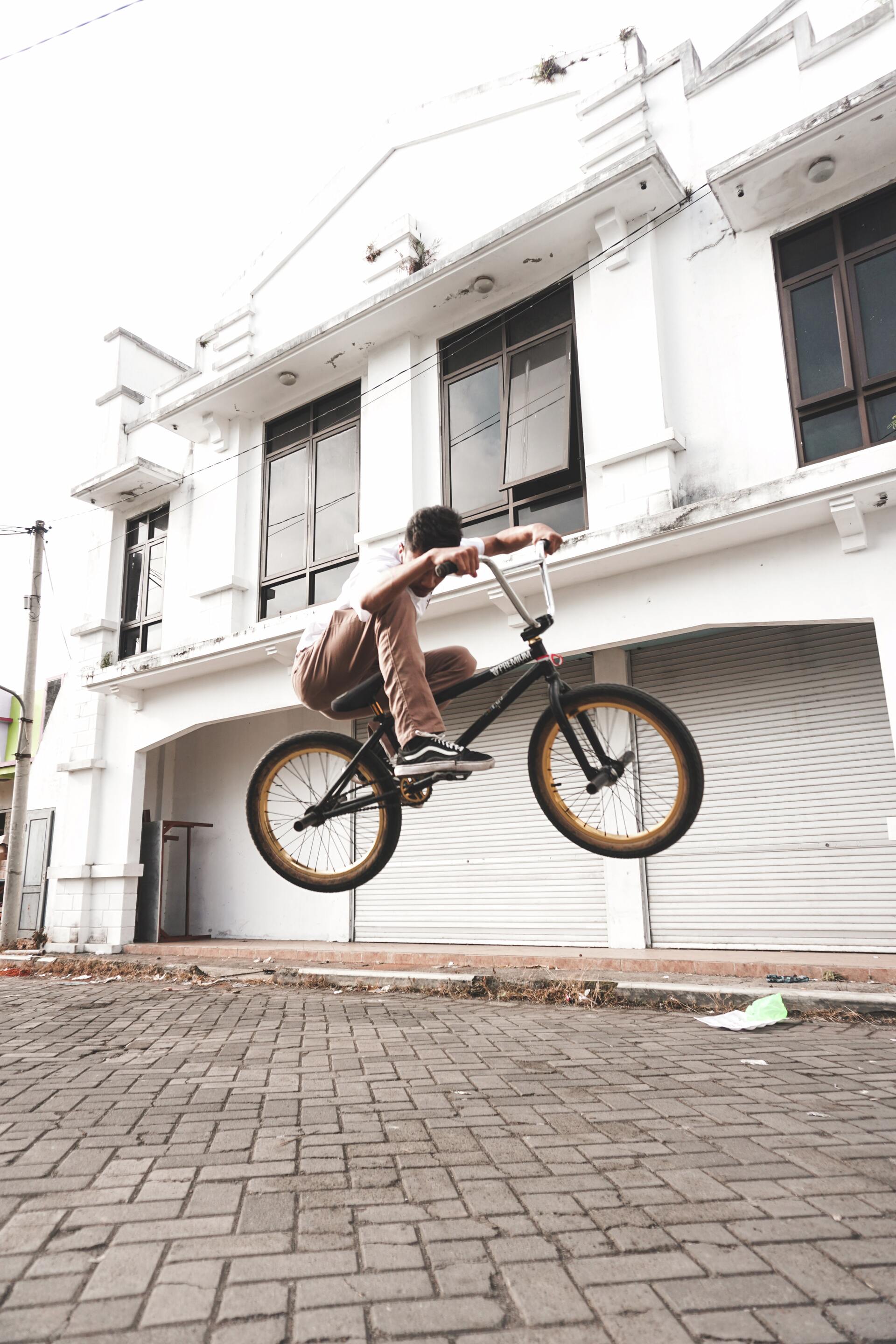 Hombre con camiseta blanca y pantalón marrón a mitad de salto en una bmx