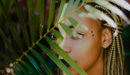 Mujer en la naturaleza atrás de una hoja de un árbol.
