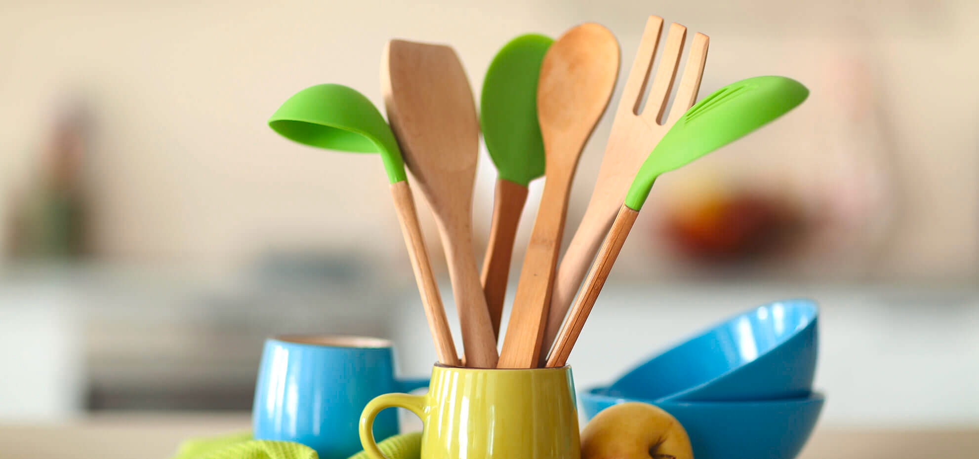 Beberapa spatula masak yang terbuat dari kayu di dalam mug hijau di atas meja dapur
