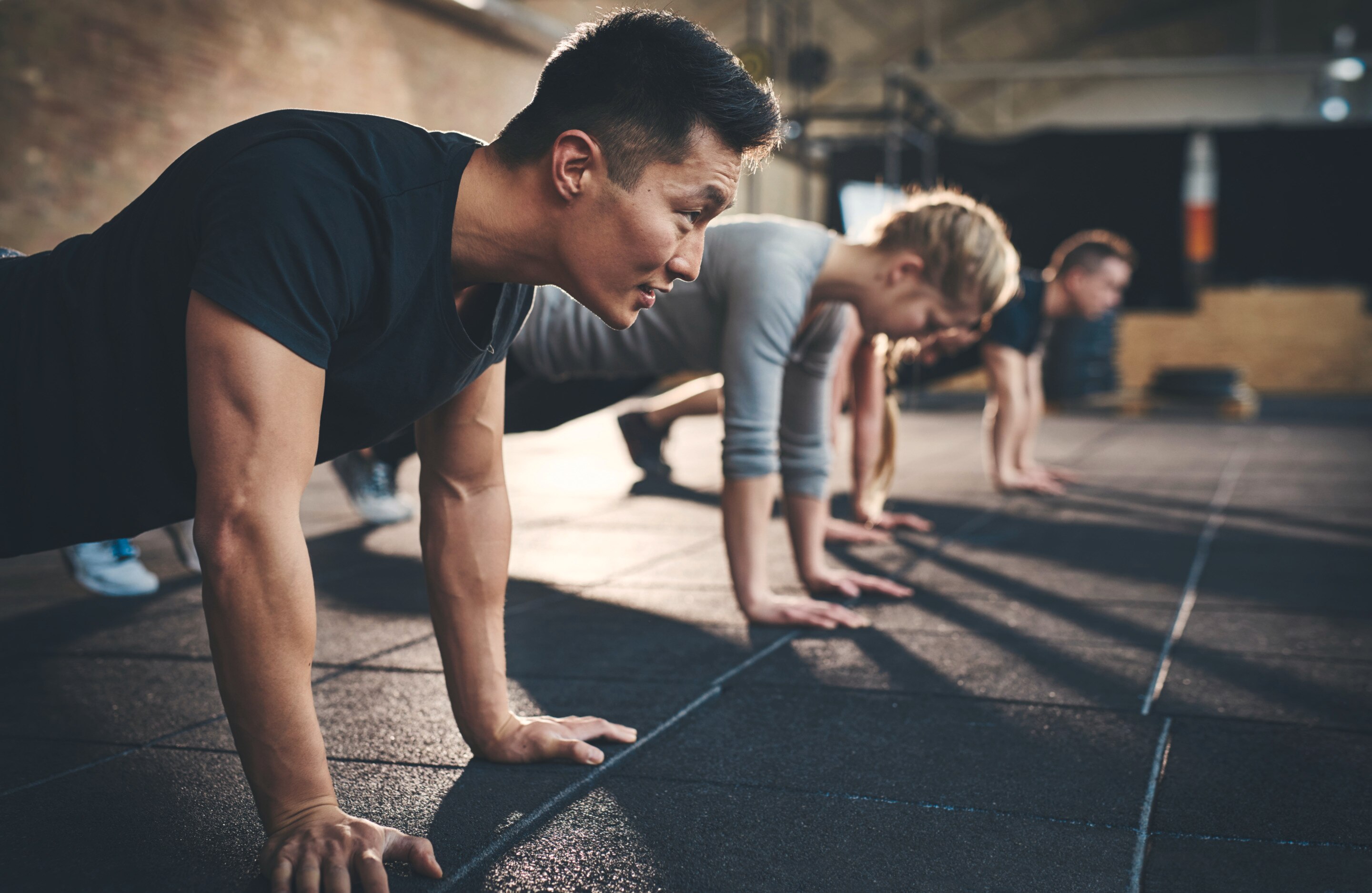 Asian man smiling while he's working out with friends and about to do a push up