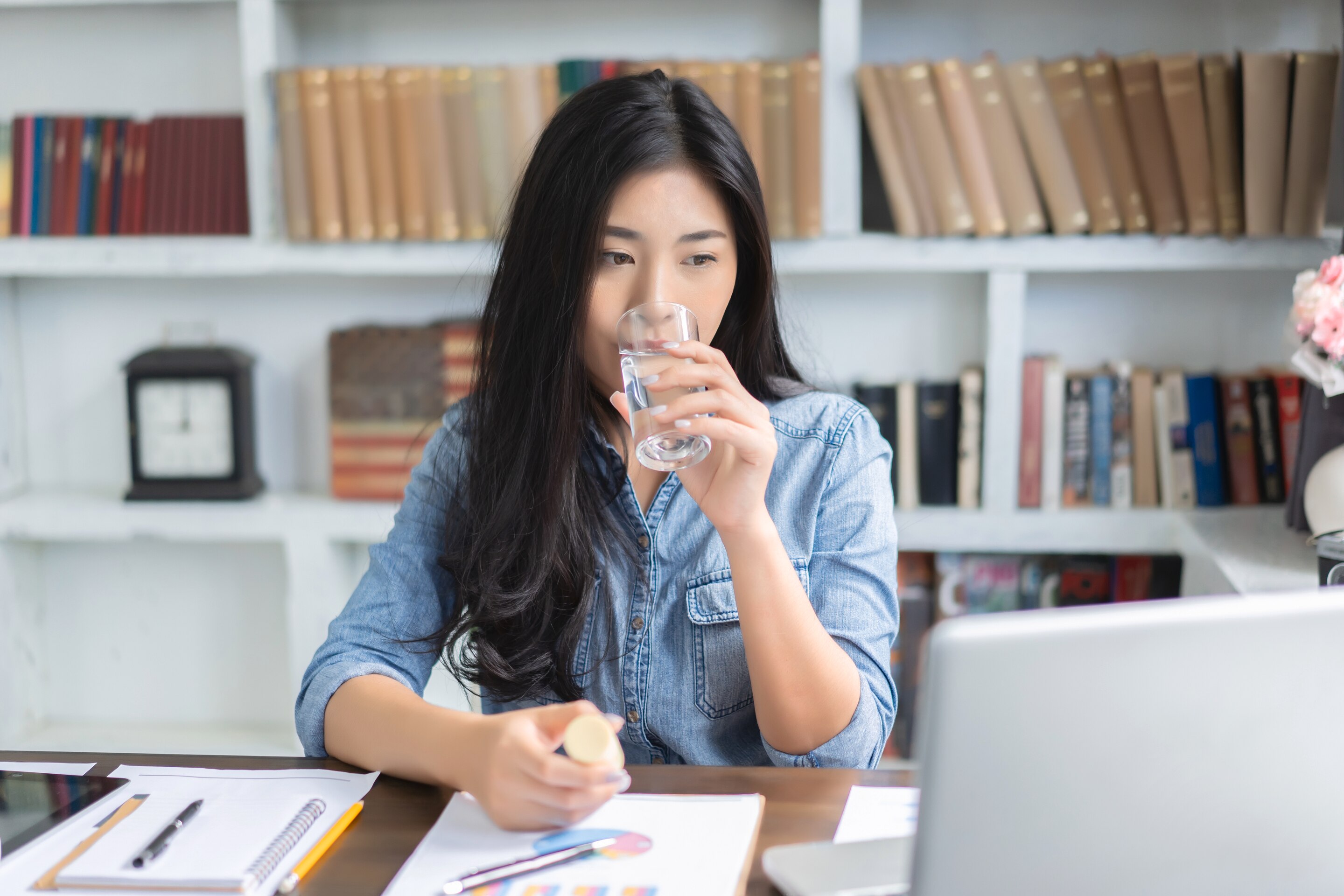 wanita asia meminum air putih sambil menatap laptop saat sedang bekerja