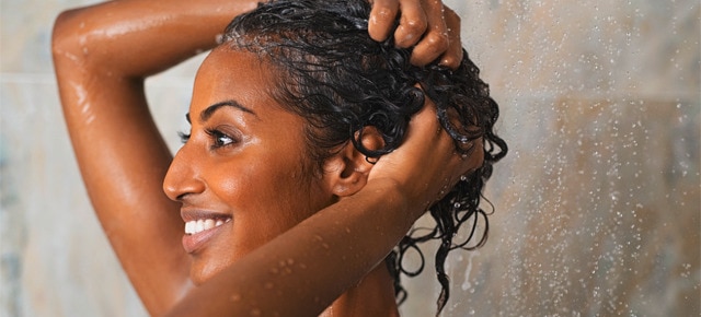 Wanita dengan rambut keriting menggunakan sampo di kamar mandi