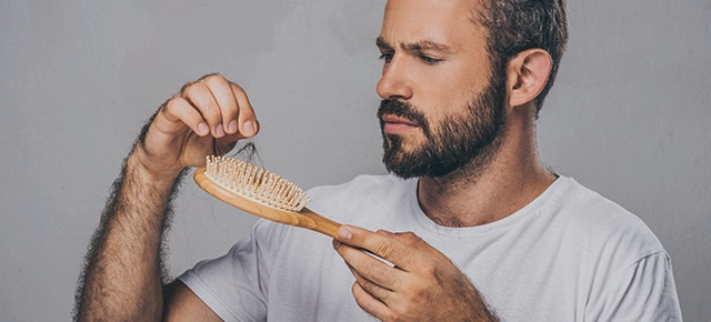Homem verificando melhora na queda de cabelo na escova